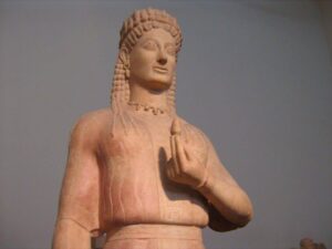 Phrasikleia wears a wreath of alternating open and closed lotus blossoms, golden lotus-bud jewelry, and holds a closed lotus bud in her hand.